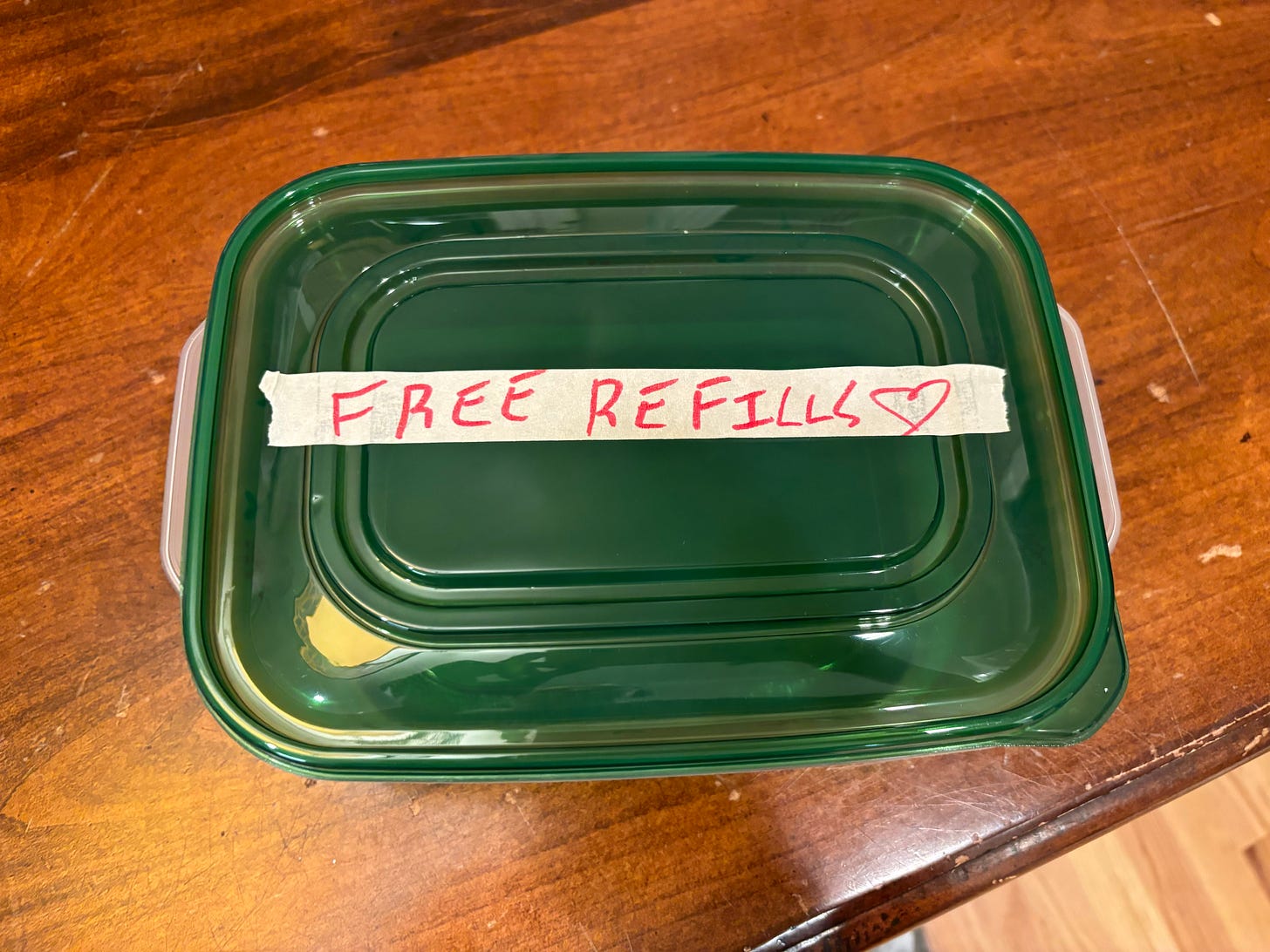 A green rectangular Tupperware with FREE REFILLS written in red on masking tape in messy handwriting