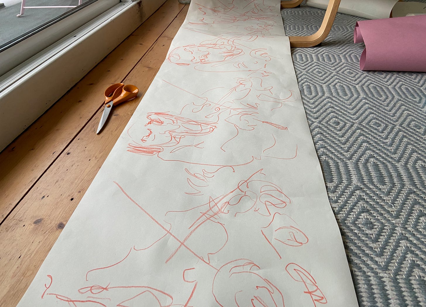 series of fast drawings of violin playing in red crayon across a roll of Ikea paper lying on a wooden floor with blue and white rug