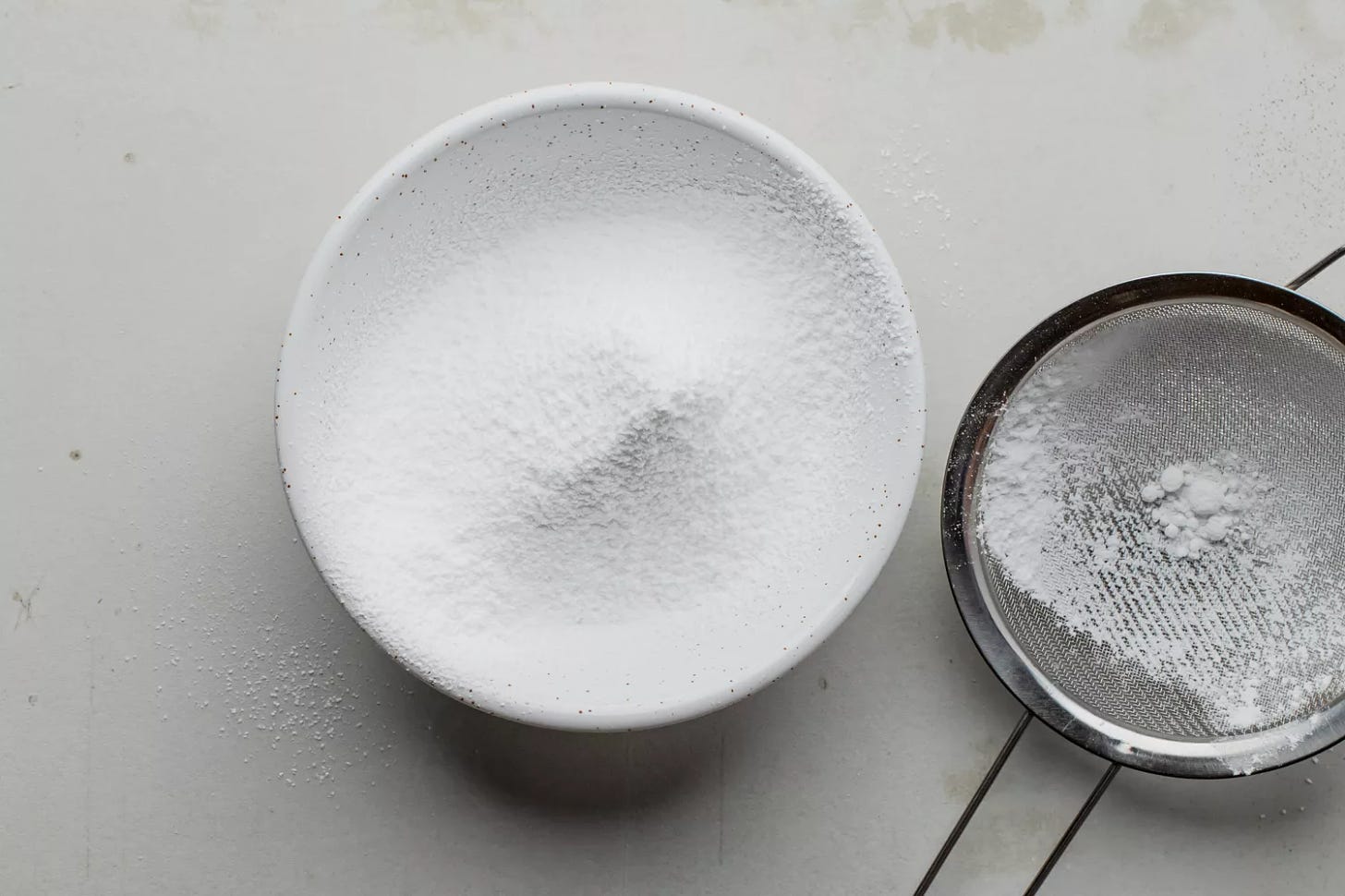 Confectioners' sugar sifted into bowl using a wire mesh sieve