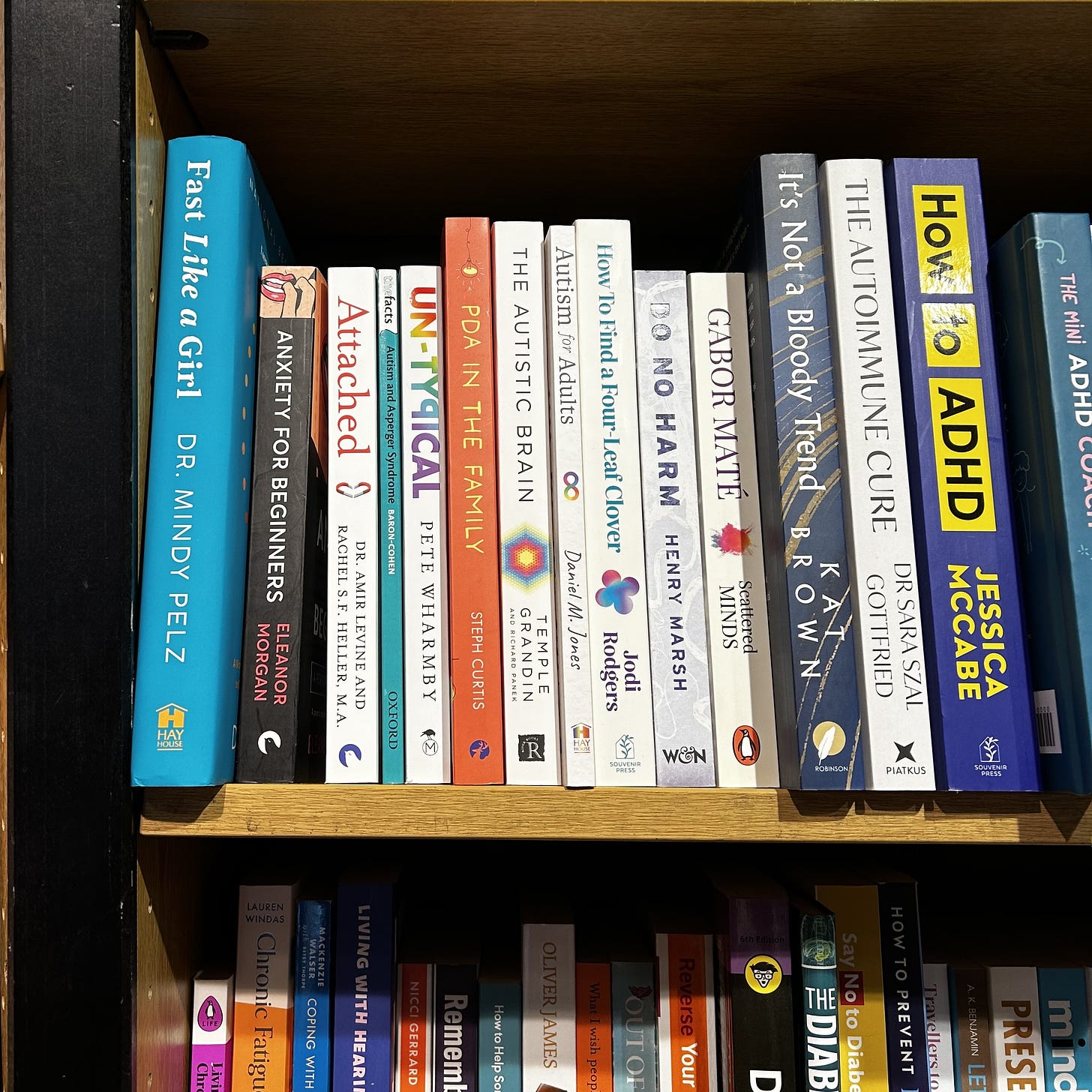 books on shelf in bookshop orange cover of pda in the family is flanked by Atypical by Pete Wharmby and the autistic brain by temple grandin