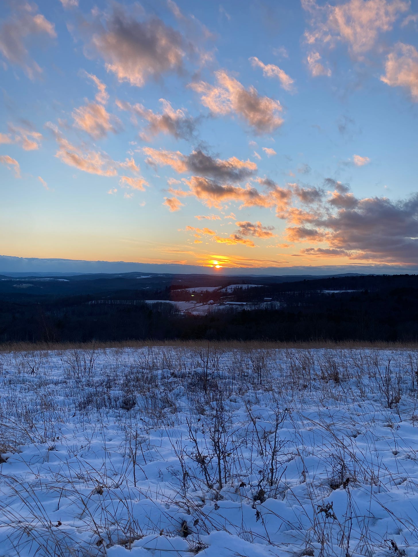 The sun setting into a bank of clouds on a snowy ridgetop.