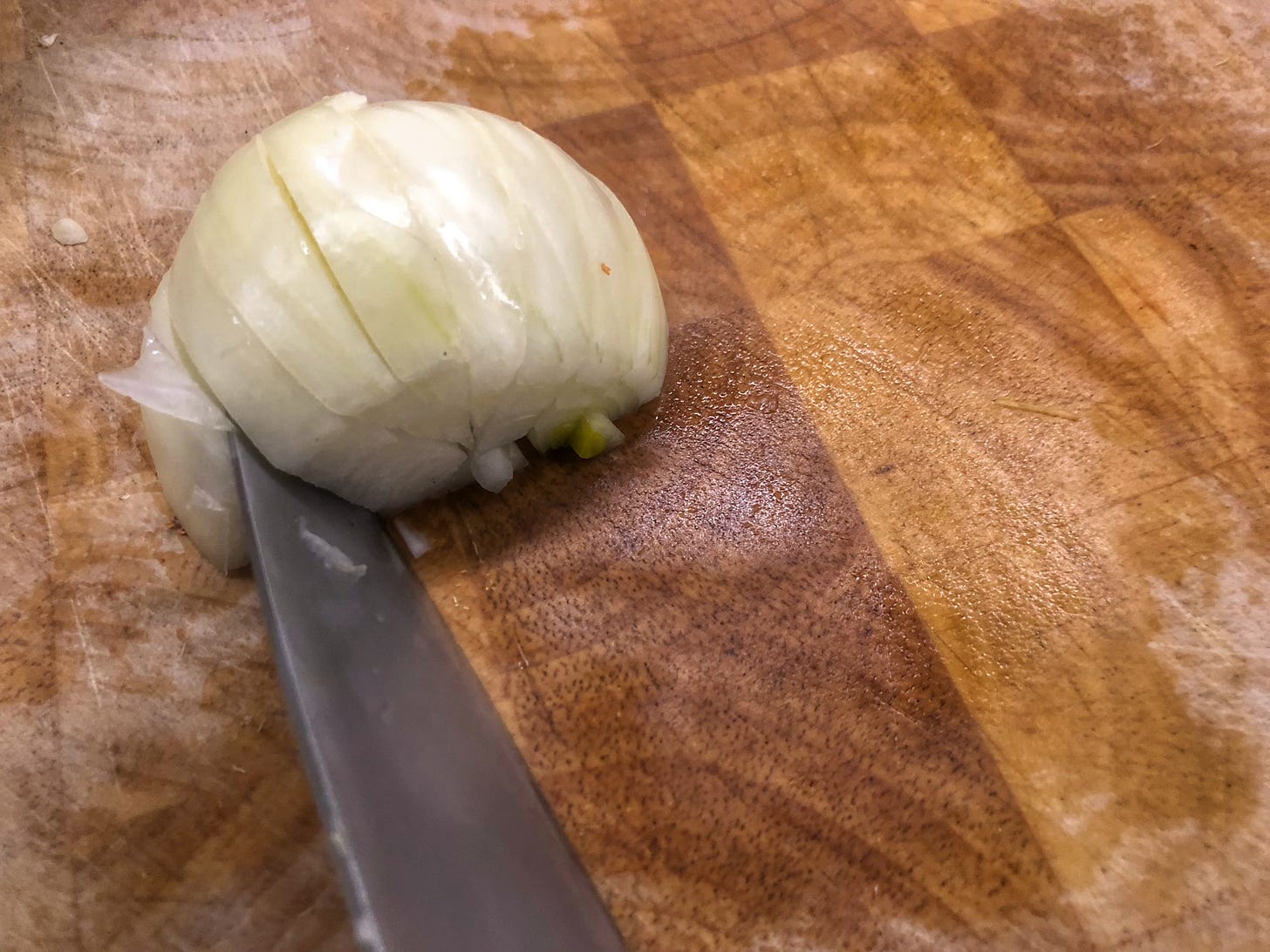 Half an onion on a cutting board, being sliced radially with a series of cuts towards its middle. 