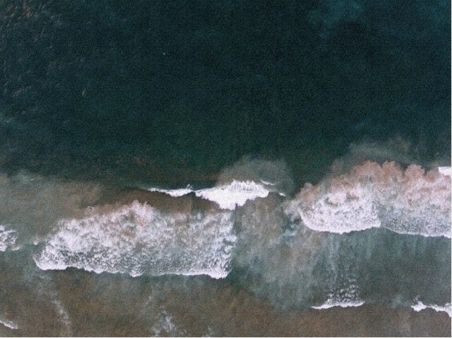 emerald-colored waves crash along the sand. the image is shot from a drone above, giving a bird's eye view. 