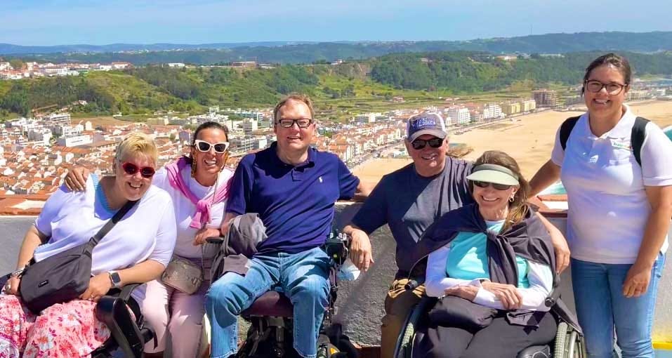 John seated next to a group of disabled travelers at a lookout point above a coastal beach.
