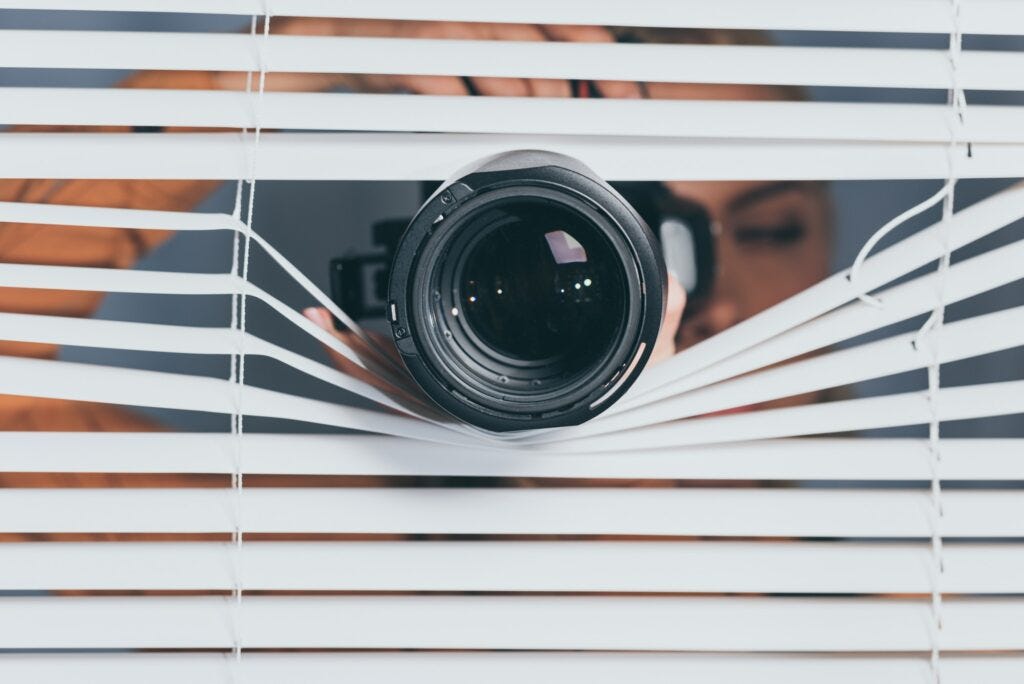 close-up view of camera and young woman spying through blinds