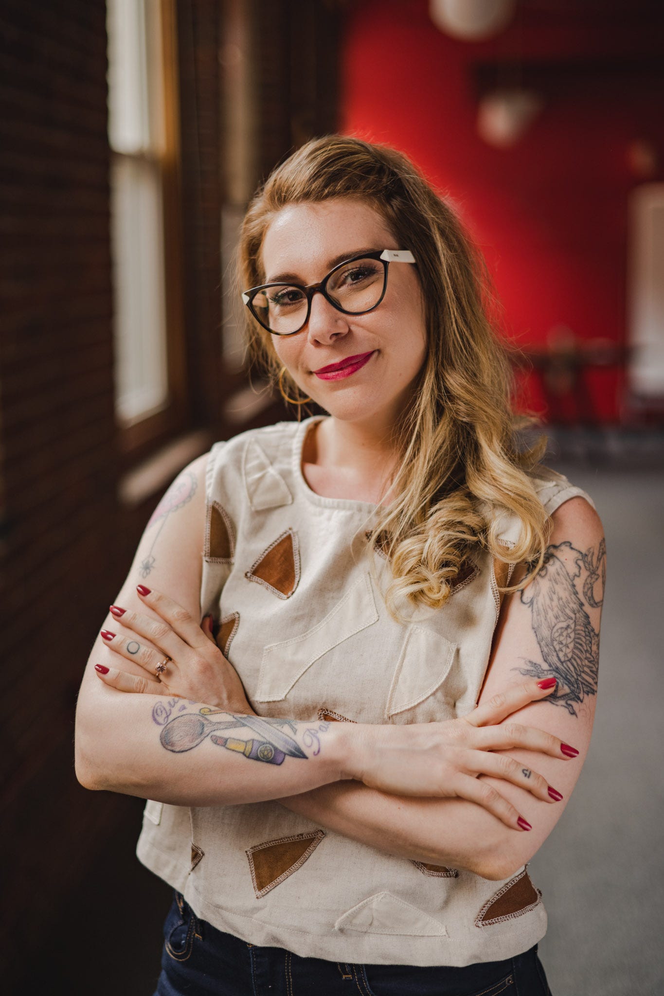 Dr. Kate is a white woman with red hair and tattoos on her arms and hands. She is smiling at the camera with her arms crossed.