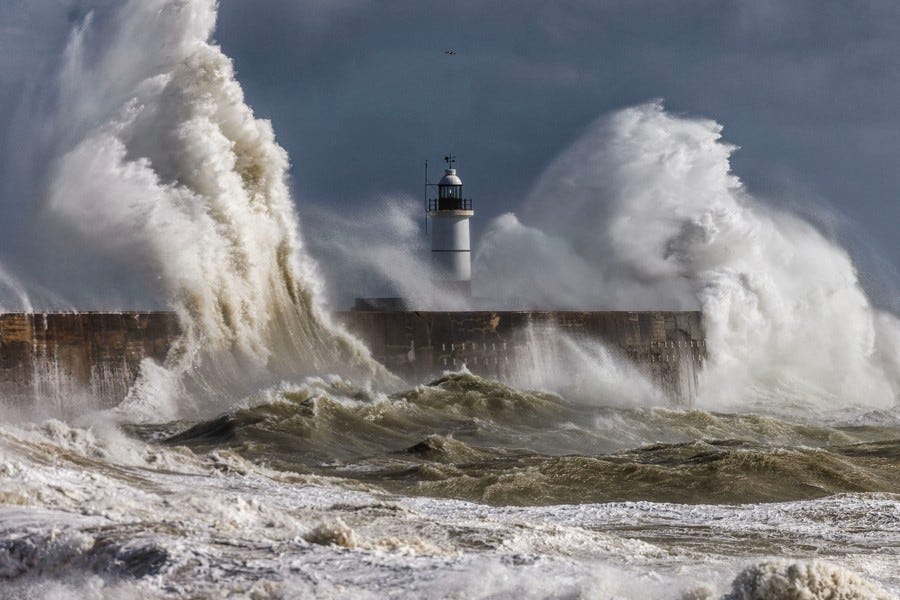 Big waves crash onto a breakwater and lighthouse.