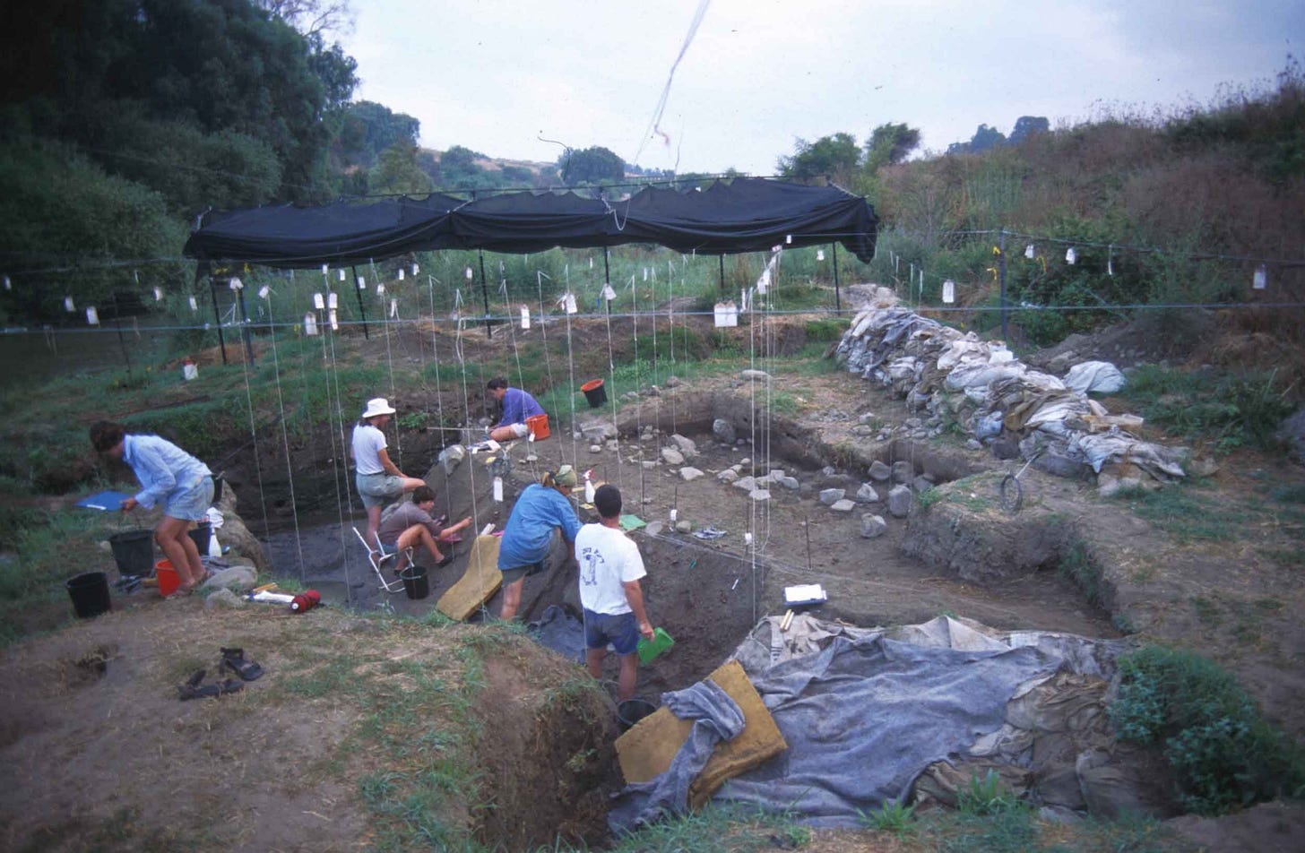 Archaeologists at work on an open air site with trenches, stones, and string grid visible