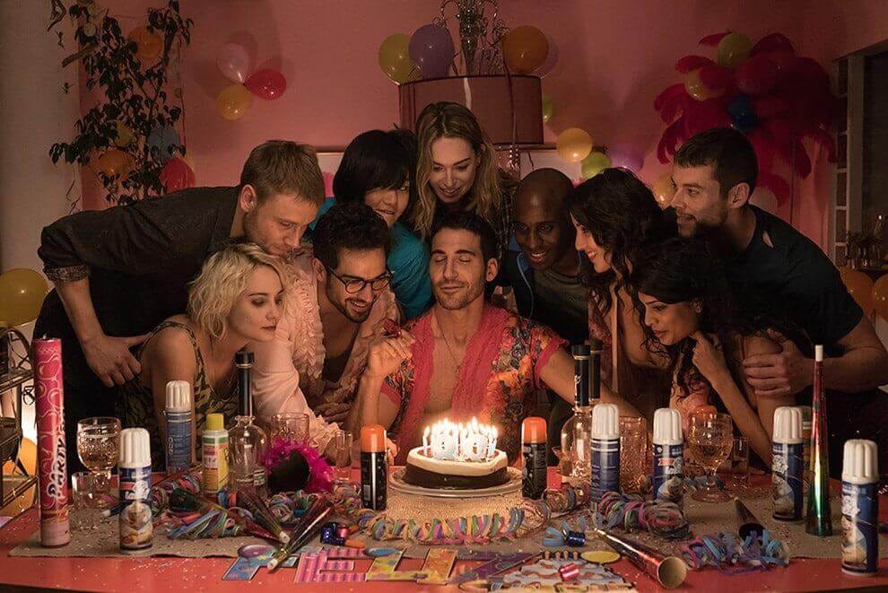 The birthday scene in Sense8 season 2, episode 1 when Lito is sitting at a table with a birthday cake full of lit candles in front of him, surrounded by his cluster and his life partners all gathering around the cake together. The room is covered in celebratory decor, the wall and table are Barbie pink.