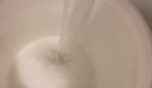 water pouring into a bucket with a soapy laundry solution