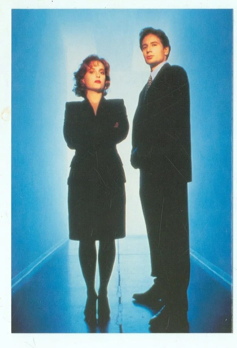 An X-Files promotional image with Mulder and Scully wearing black suits against a blue background
