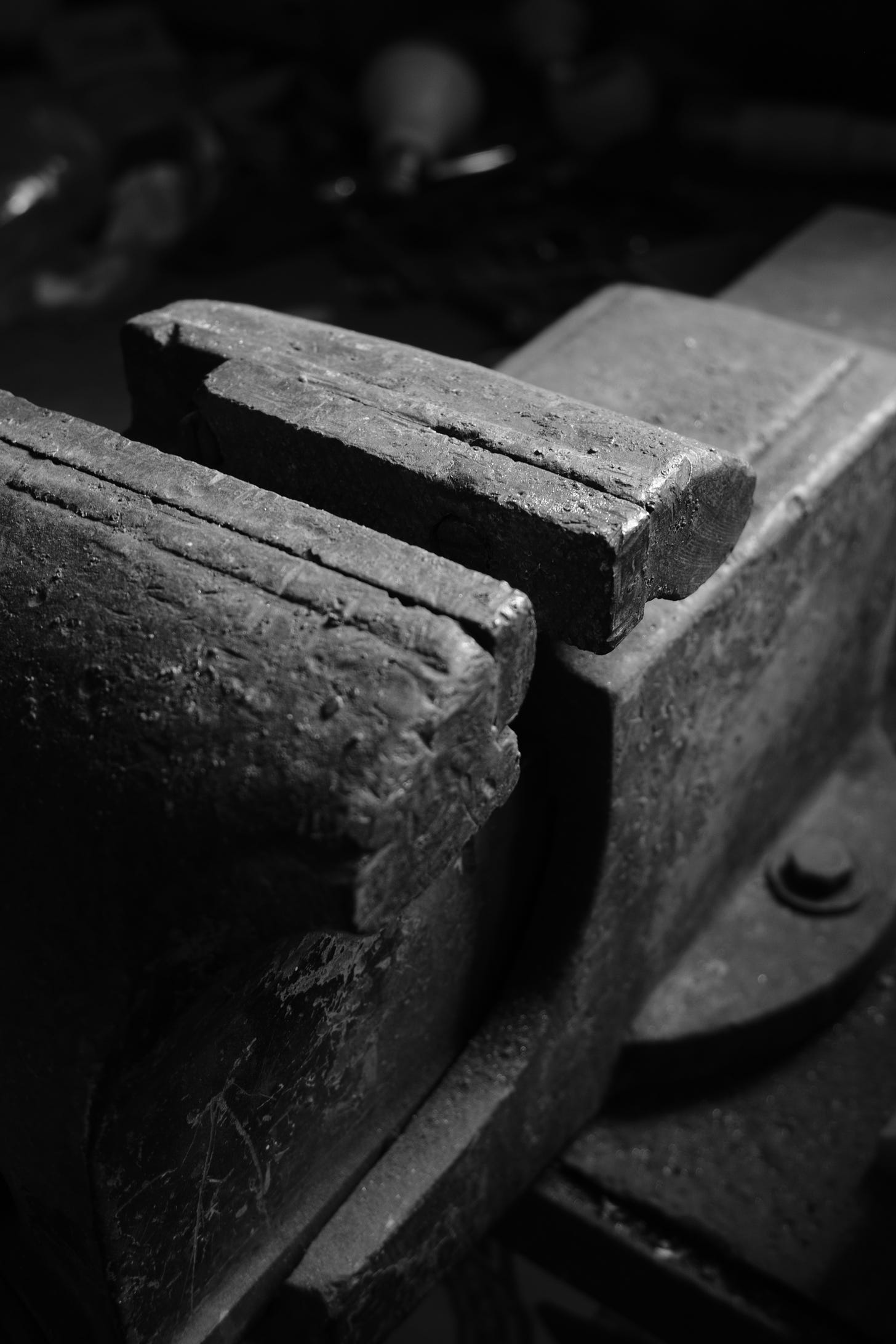 A black and white photo of a metal vise with a piece of wood in between.
