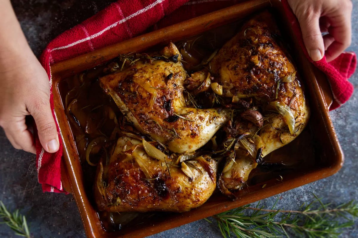 a person serves a large tray. of pollo al horno beside somw fresh sprigs of rosemary