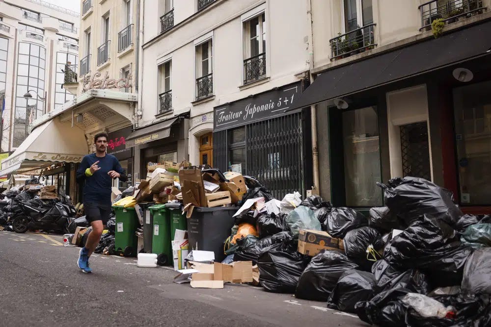 A man jogs past uncollected garbage bags Tuesday, March 28, 2023 in Paris. A new round of strikes and demonstrations is planned against the unpopular pension reforms that, most notably, push the legal retirement age from 62 to 64. (AP Photo/Thomas Padilla)