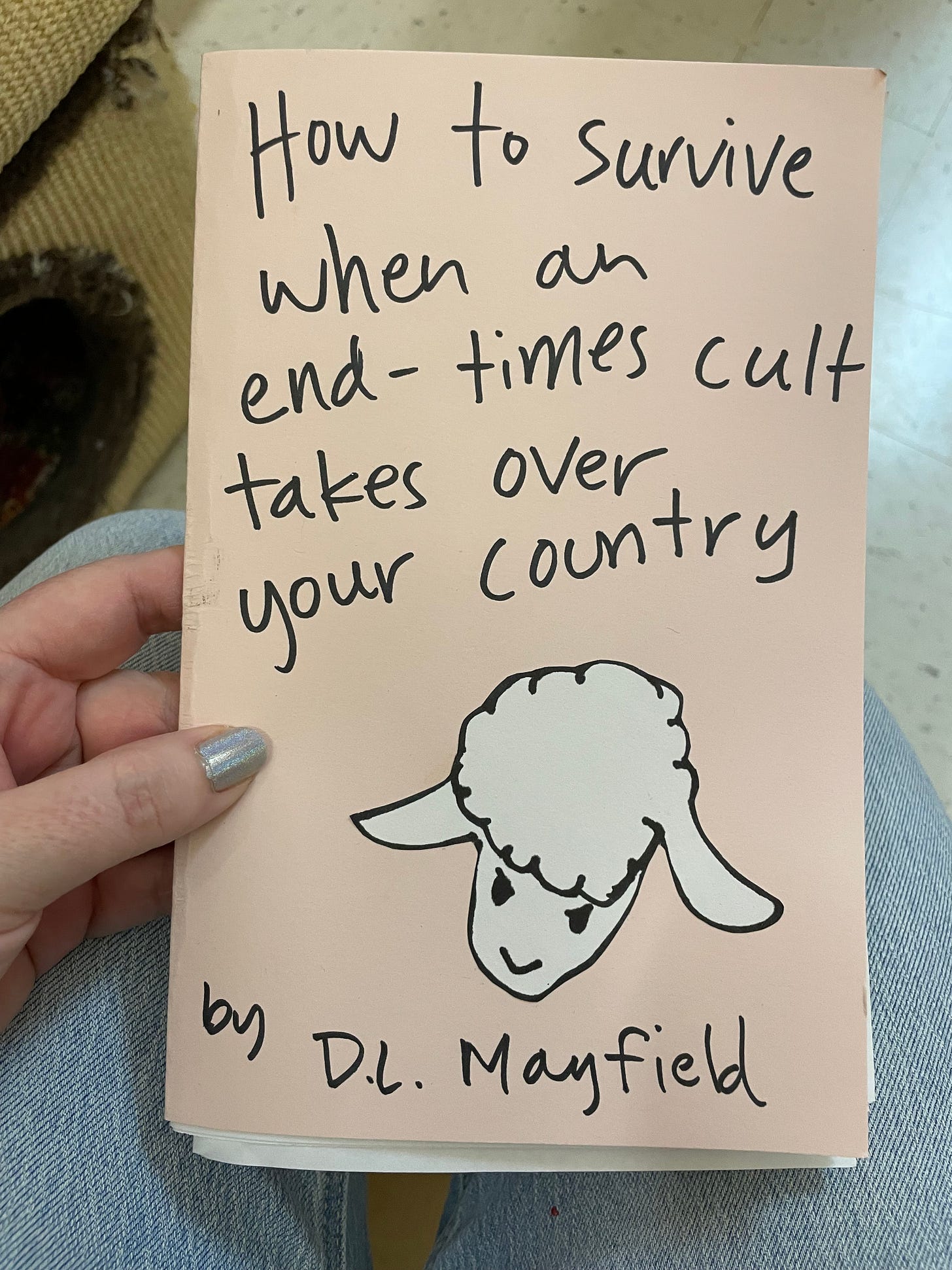 pink paper zine cover in black handwriting it says how to survive when an end times cult takes over your country by dl mayfield. there is a drawing of a lamb on the front