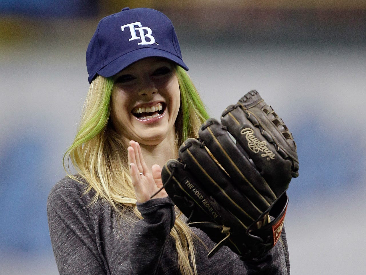 Avril Lavigne in a TB hat, laughing and holding a glove after throwing the ceremonial first pitch