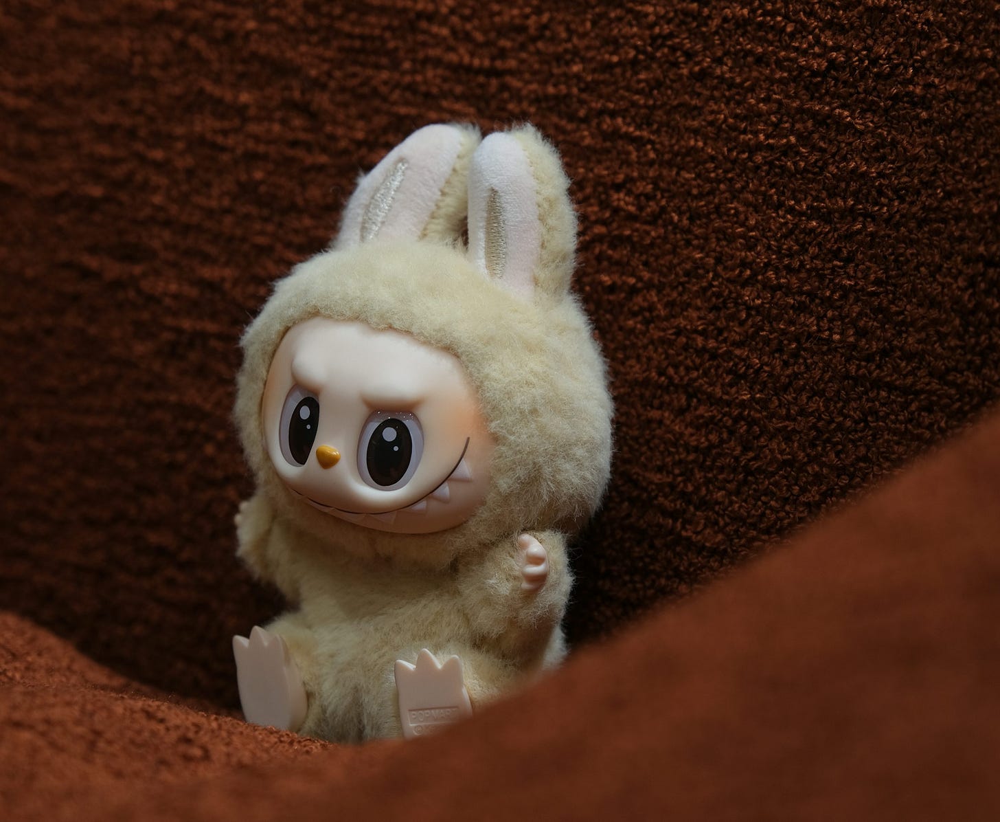 A toy bunny doll sits on a brown surface.