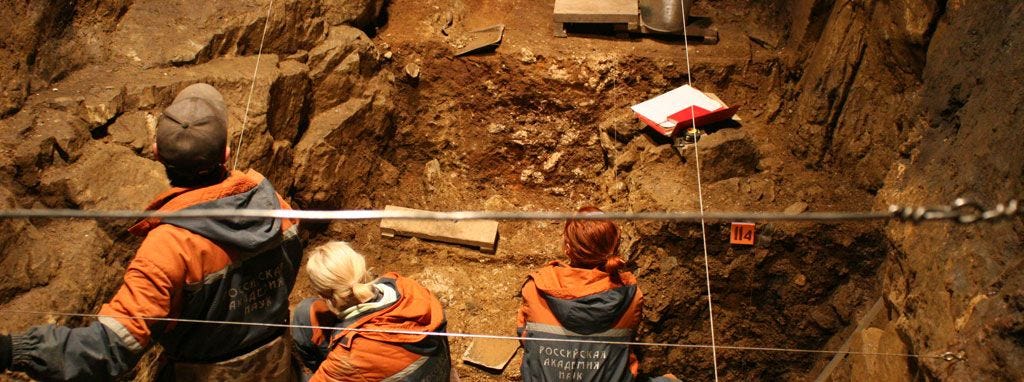 Three archaeologists working in a cave site with sediment profile