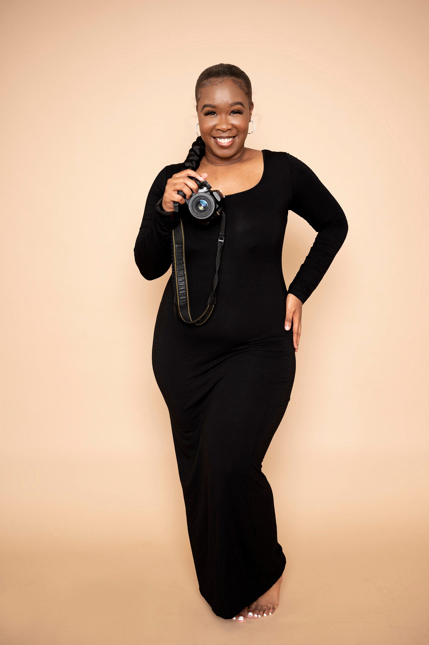 Young black woman in long black dress with camera