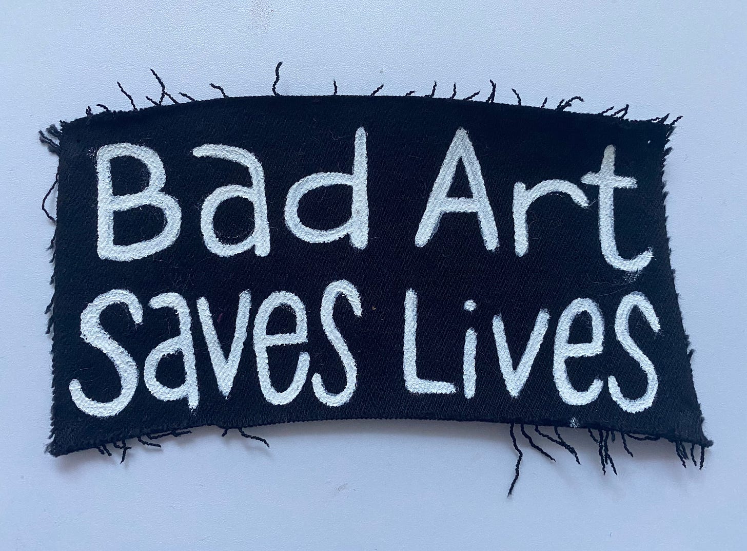 A black patch with "Bad Art Saves Lives" painted on it in white.
