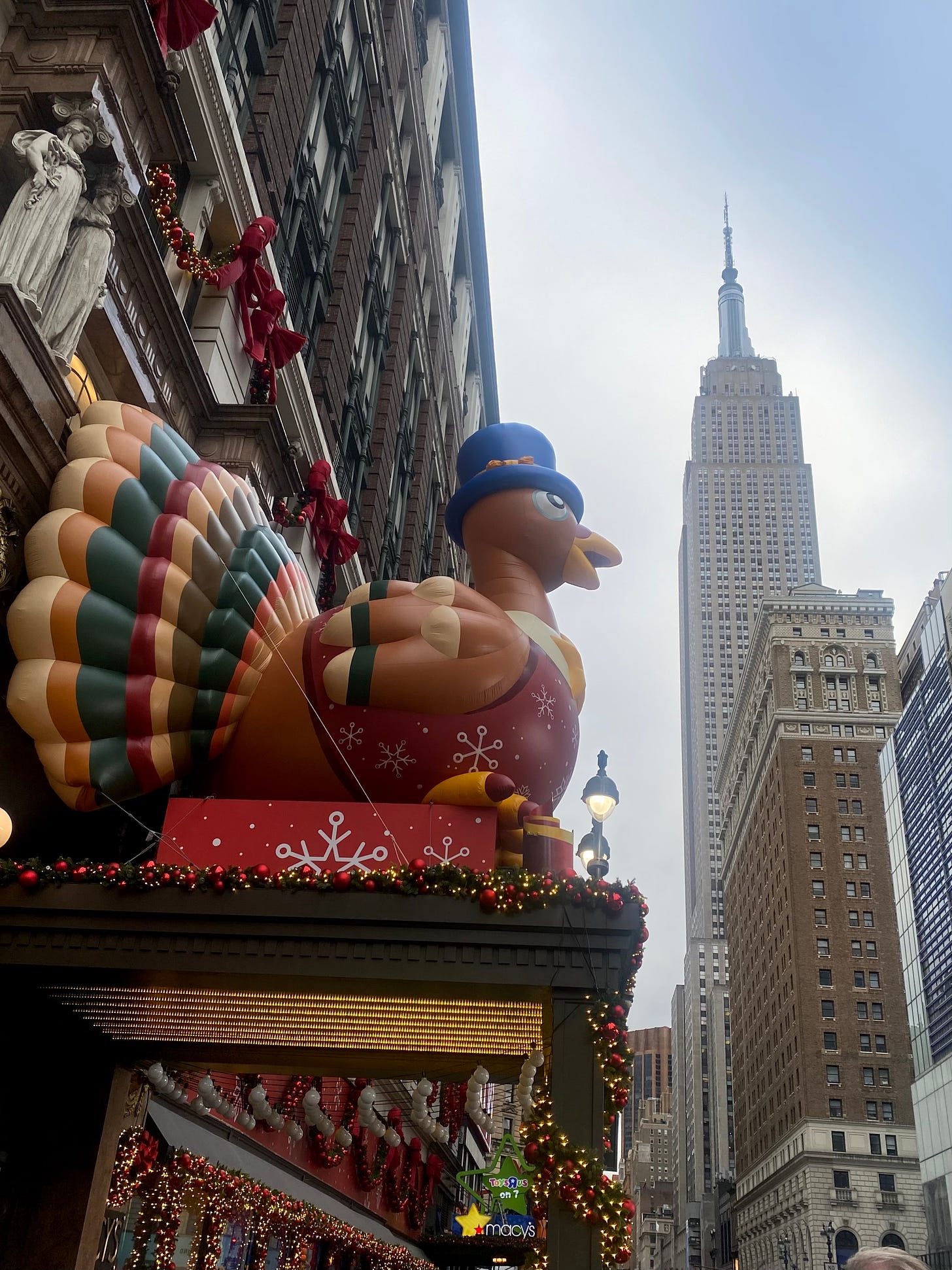 The entrance of Macy's with a giant decorative turkey over the entrance looking towards the Empire State Building.
