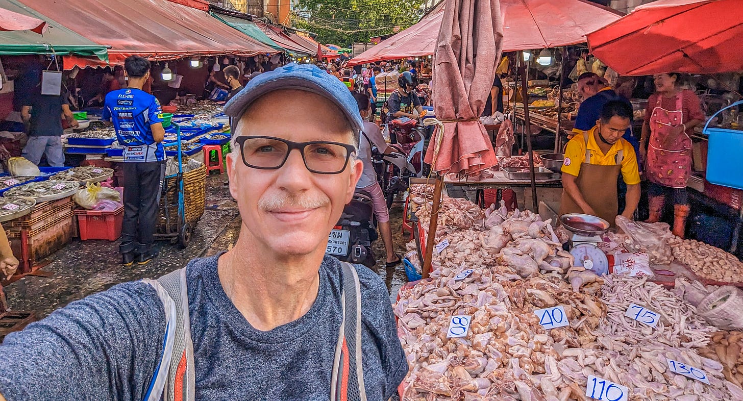 A sweaty looking Michael standing in the meat section of the market with a LOT of chicken right behind him. 