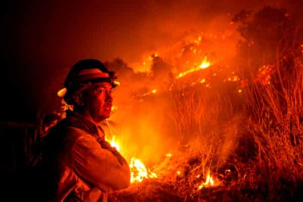 A firefighter watches a nighttime fire on a hill. A firefighter watches a nighttime fire on a hill.