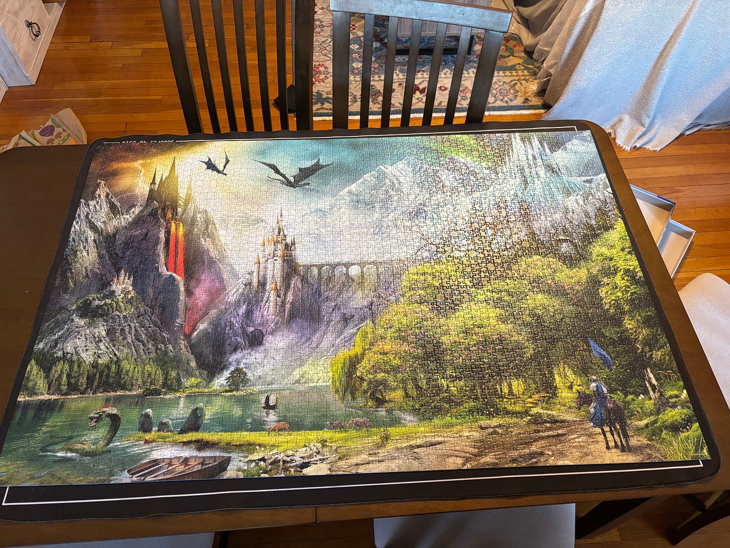 3,000 piece puzzle of a fantasy scene, with a rider on horseback at the base of a mountain path to a castle with dragons in the air and a sea monster in the water.