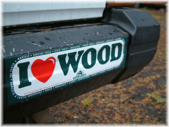 A bumper sticker that says I (heart) wood, on the back of a white vehicle