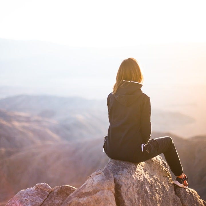 person sitting on top of gray rock overlooking mountain during daytime person sitting on top of gray rock overlooking mountain during daytime