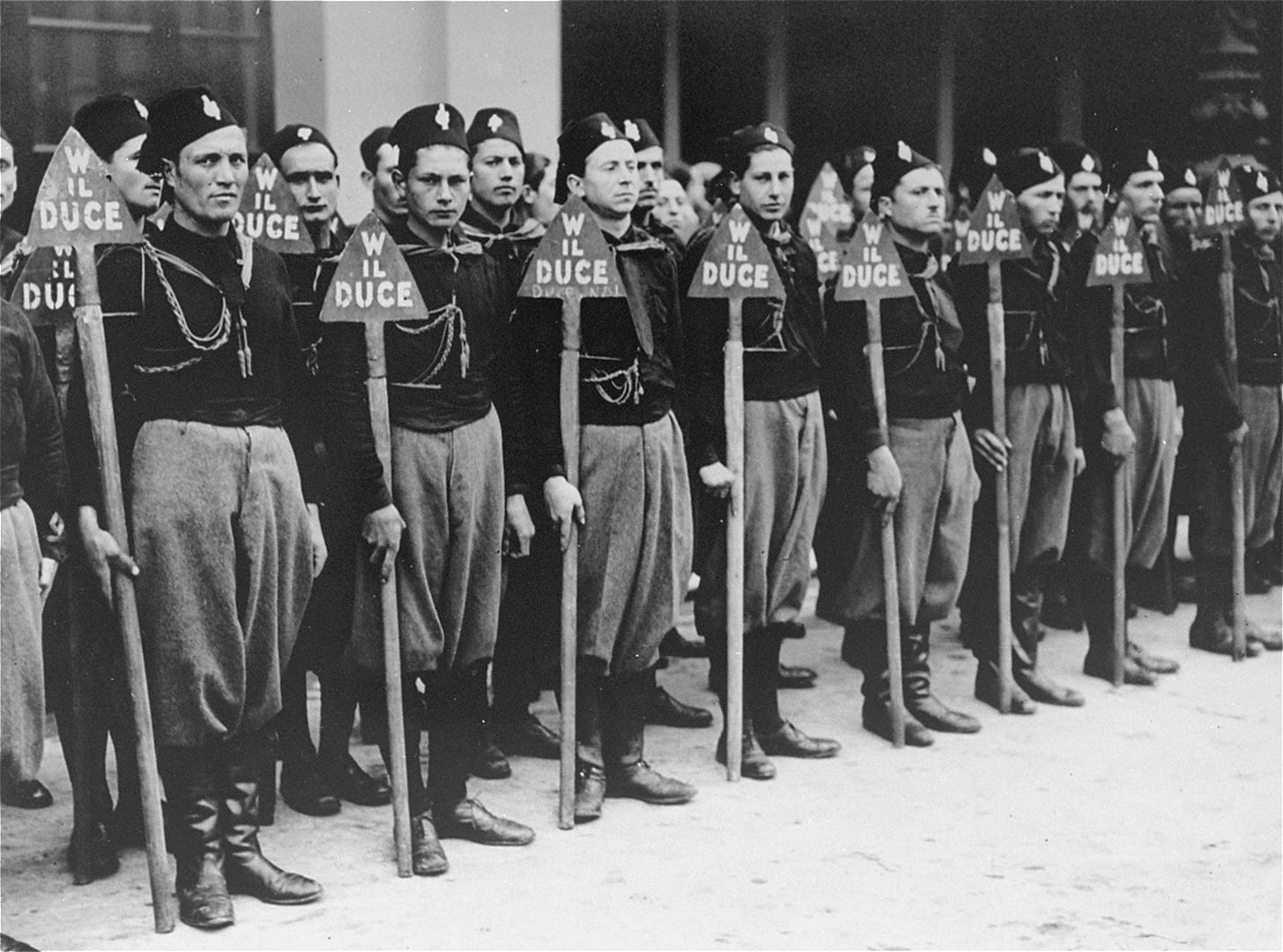 A unit of Italian blackshirts stands at attention holding spades during a fascist demonstration.