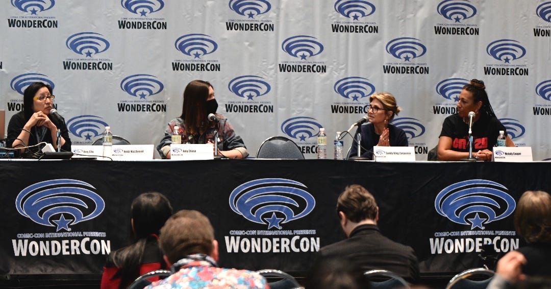 From left to right, Amy Chu, Amy Chase, Sandy King Carpenter, and Melody Cooper- four women sitting on a panel at a Wondercon ballroom stage having a conversation.