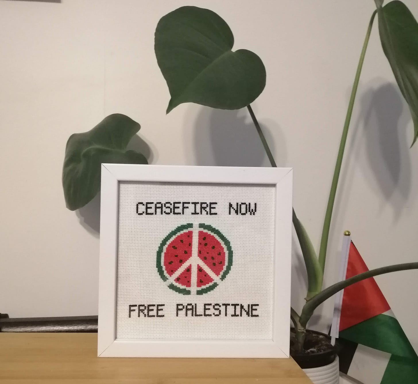 Cross stitch in a frame with the text "ceasefire now", a watermelon with the peace symbol through it and the text "free Palestine"