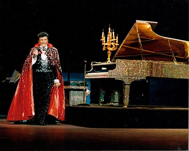 Photograph of Liberace in full regalia on stage.