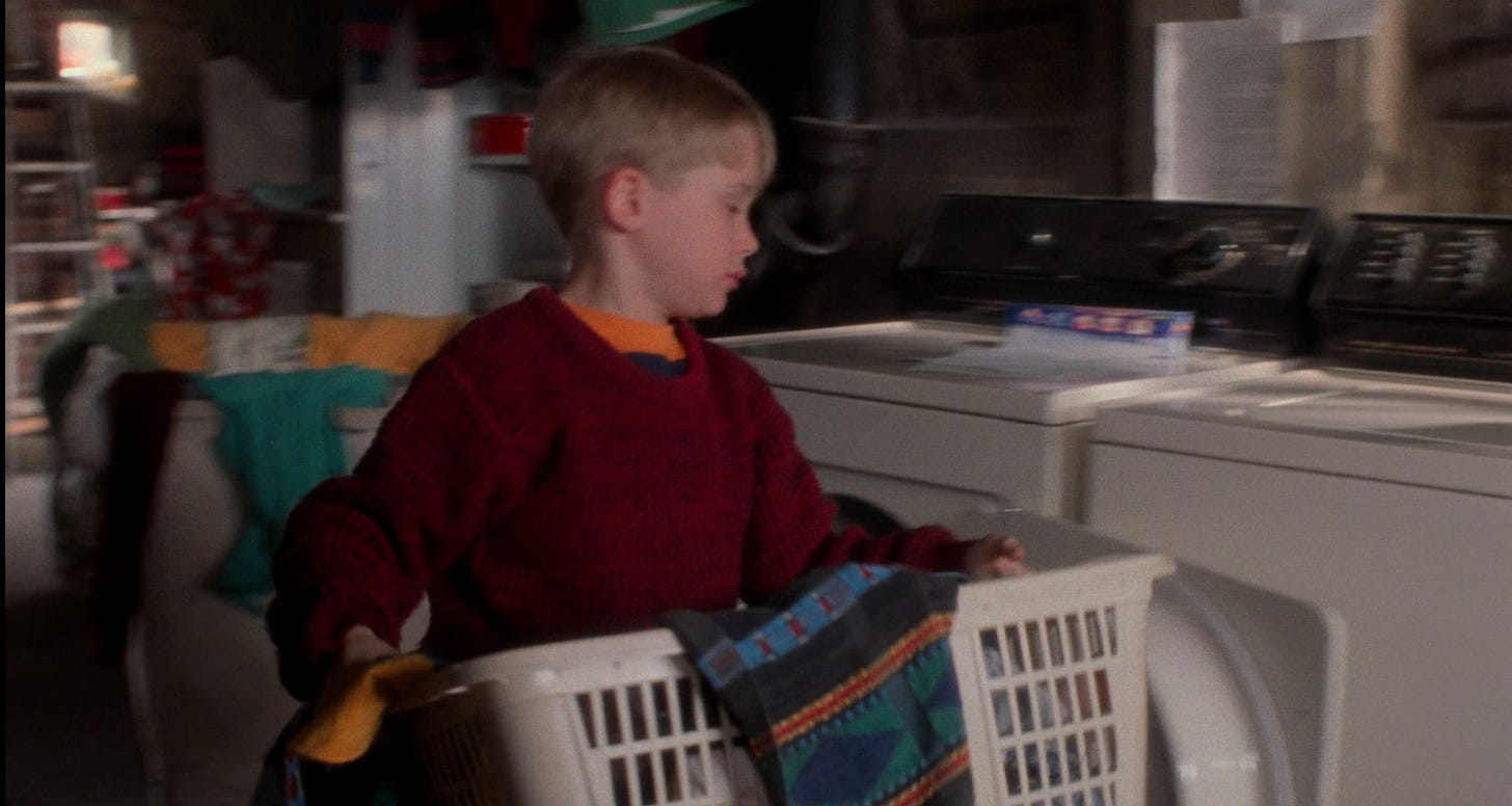 A dark basement with stuff around; Kevin McAllister is doing his laundry in this screenshot. The washer/dryer are old and white and he has an old white laundry basket.