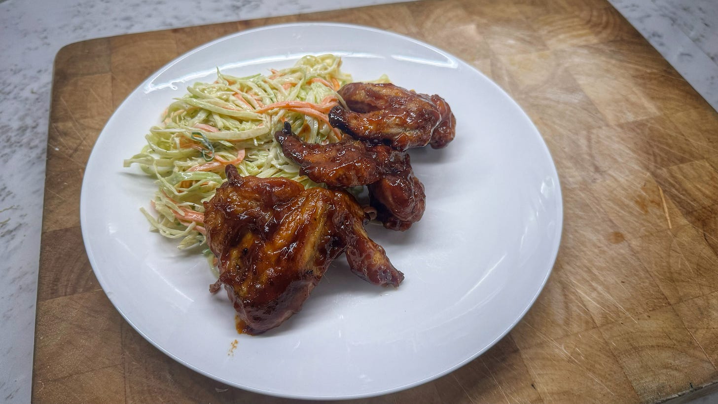 Three cooked and sauced wings plated beside some cole slaw