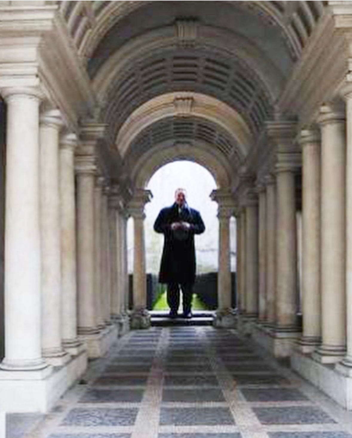 Man standing at the end of Boormini's gallery with columns and paved floor in Rome