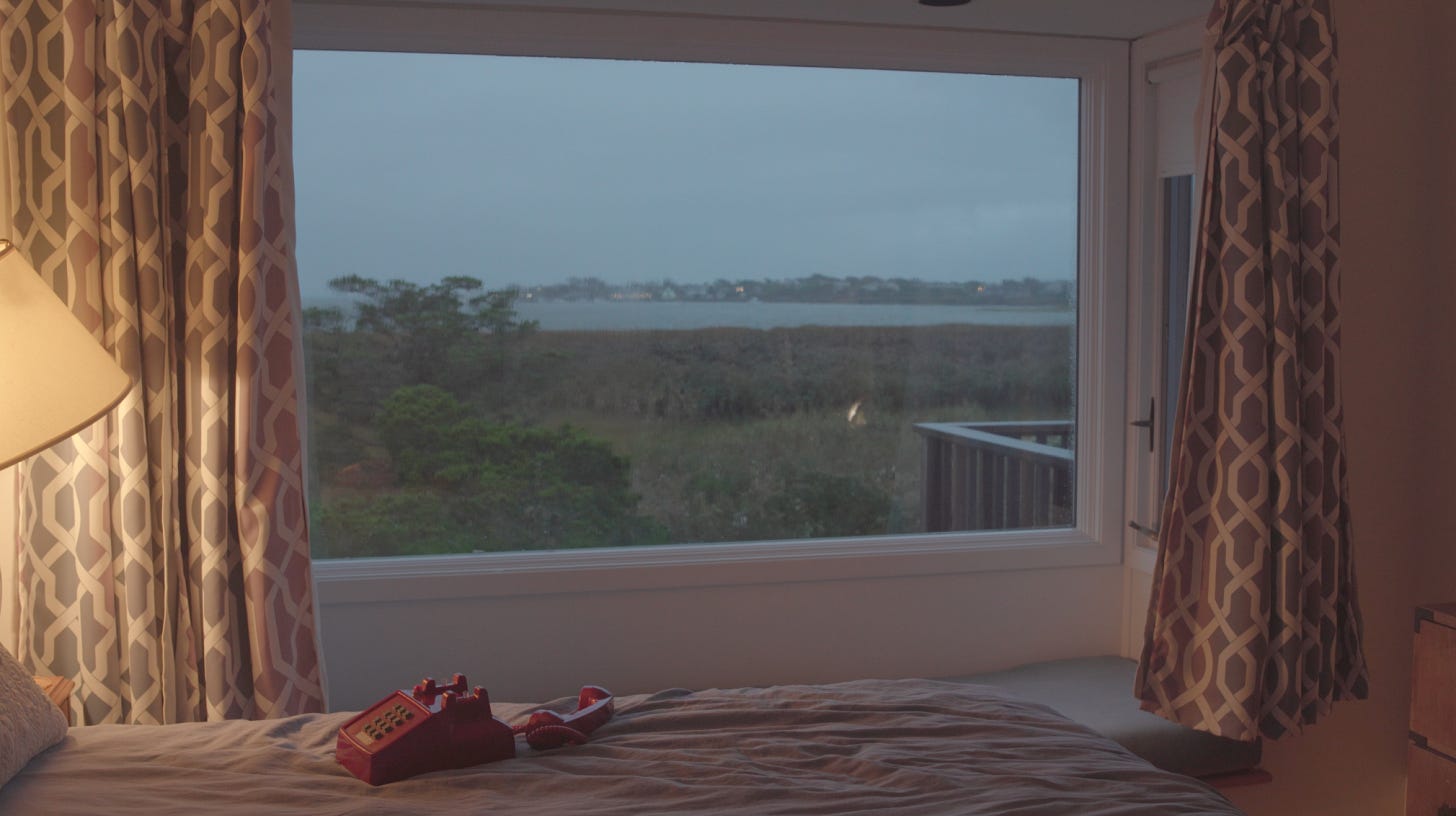 An old-fashioned red phone prop sits on a bed in front of a large window in this behind-the-scenes set photo.