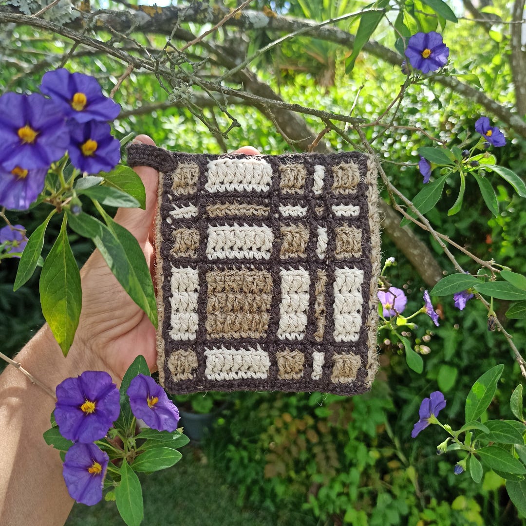 Mosaic crochet pot holder with cotton and jute, in 3 colors, in the middle of a tree's purple flowers.