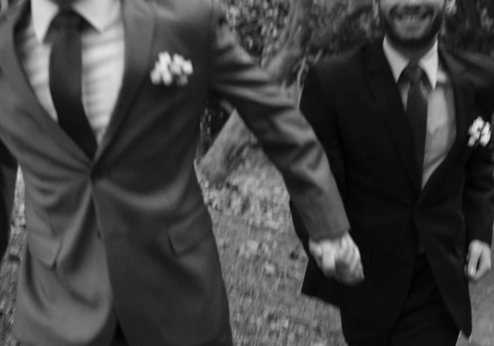 Gay couple in wedding suits running together holding hands