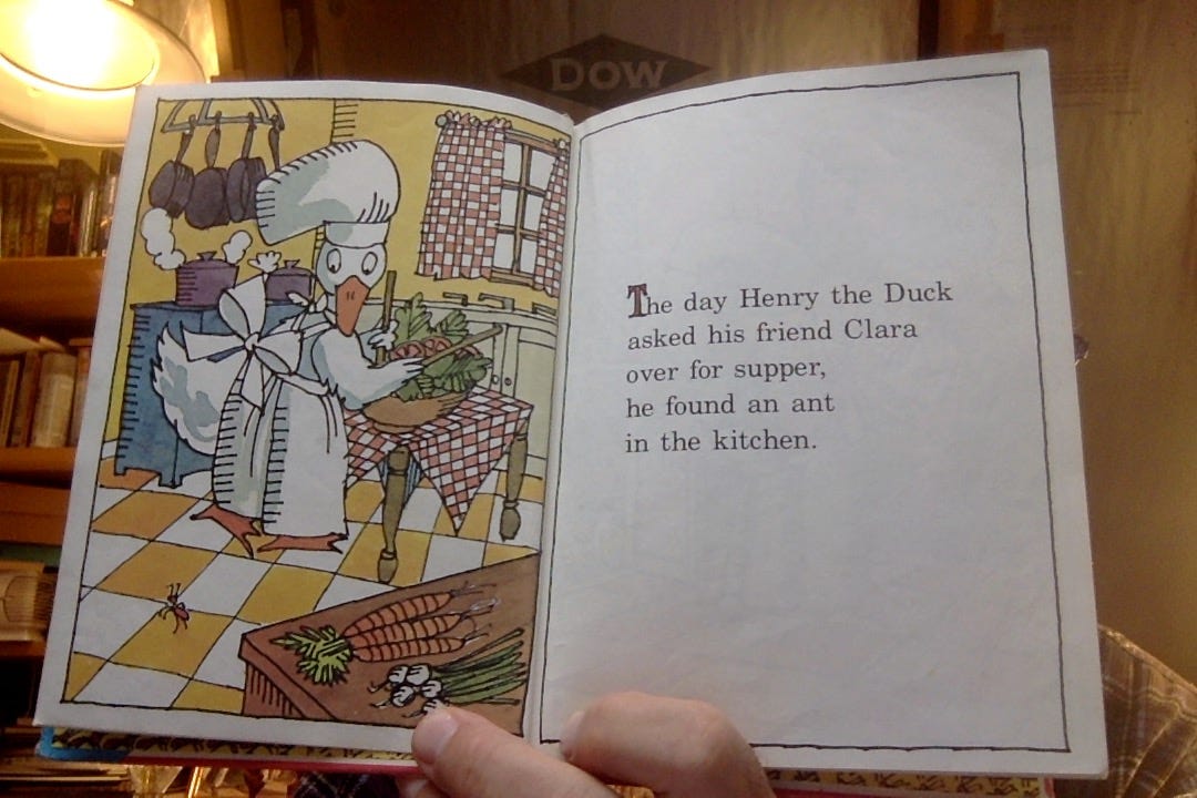 A drawing of a white duck wearing a white cap and a white apron preparing some food in a nice, if simple, kitchen. The caption reads, The day Henry the Duck asked his friend Clara over for supper, he found an ant in the kitchen. Looking closely again at the picture we can see an ant crawling near Henry's feet.