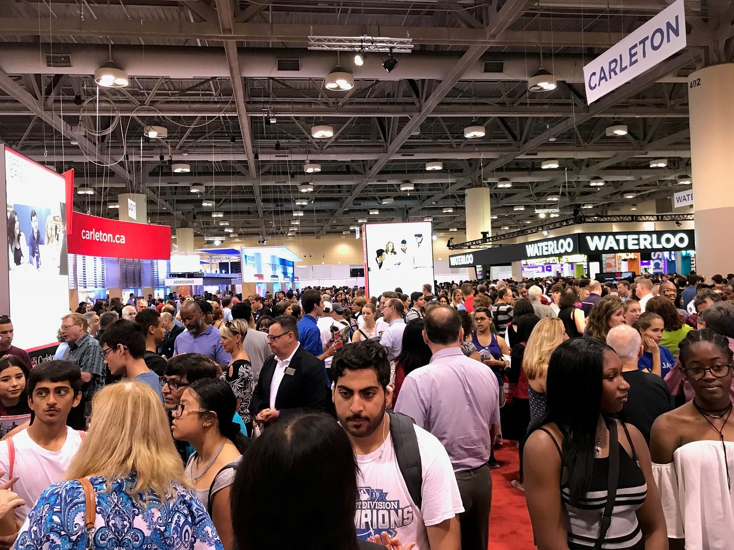 A crowded exhibition hall with university booths.