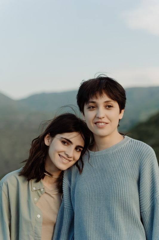 A shorter person leaning their head on a taller person's shoulder, both smiling