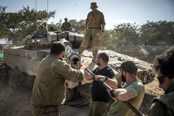 Soldiers clean the barrel of a military tank’s gun.