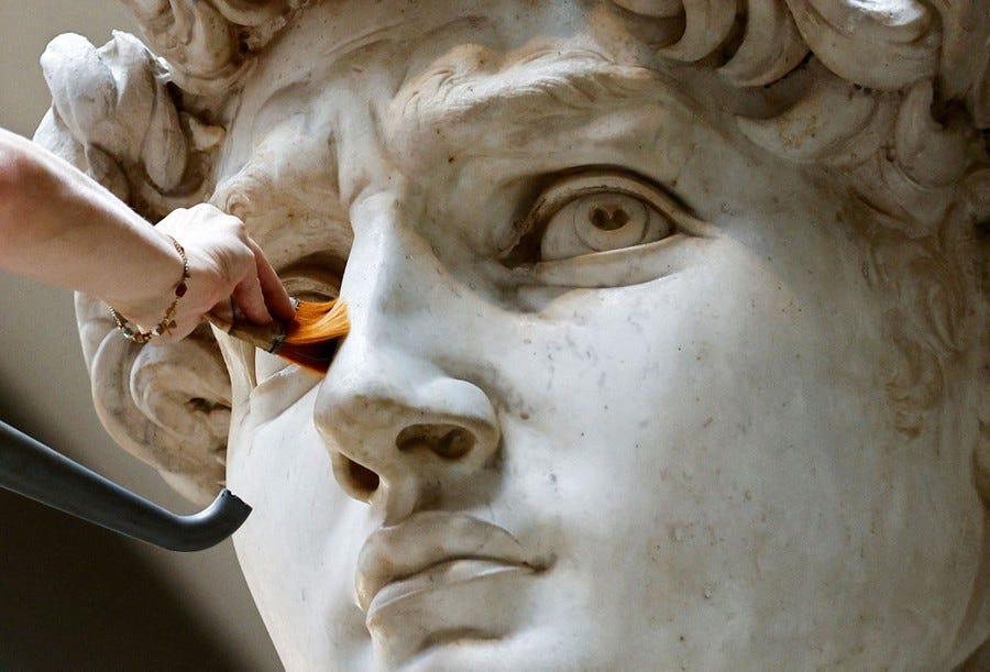 A person uses a brush to clean the face of a huge marble statue.