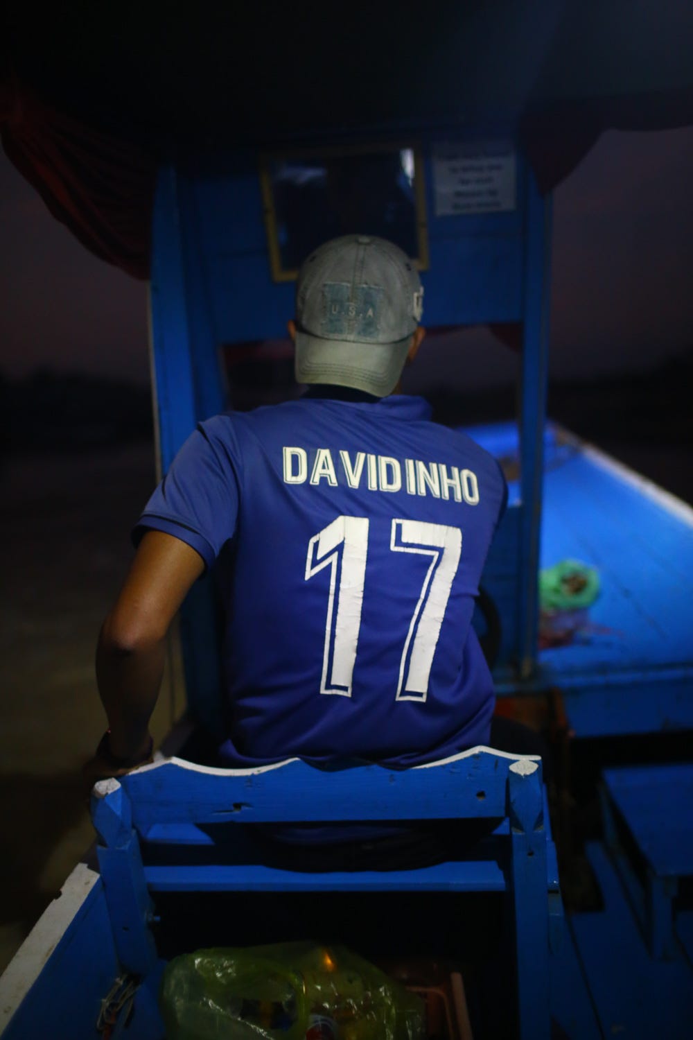The boat driver, Davidinho, is shown from behind. His back is lit to show his soccer jersey, but the rest of the scene is dark. It is night. It is terrifying.