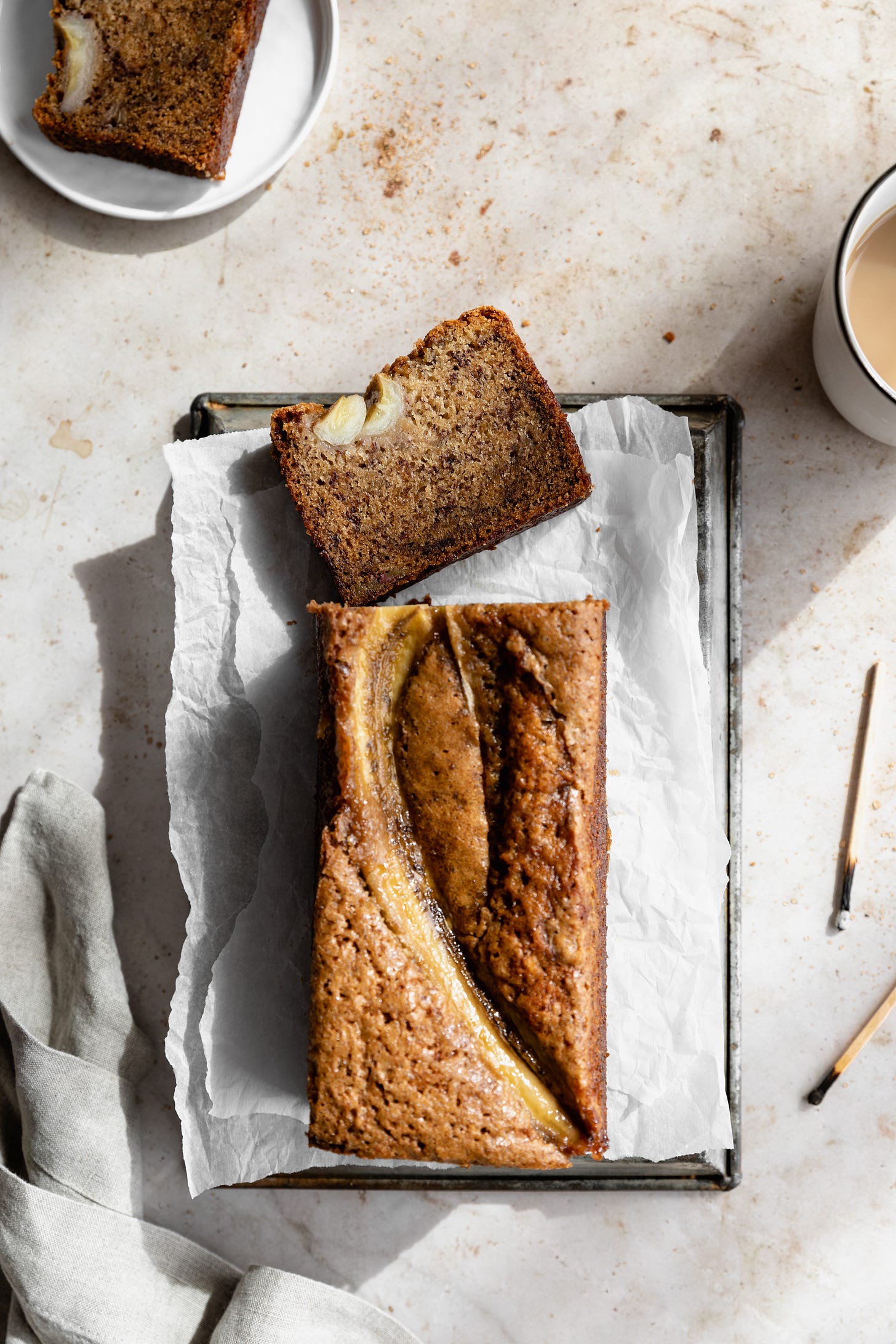 Vegan bananas foster bread with slice on metal tray on counter with coffee cup