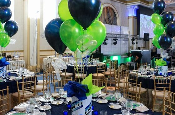 Hall filled with round tables decorated in blue, white and green with balloons, set for a teen party