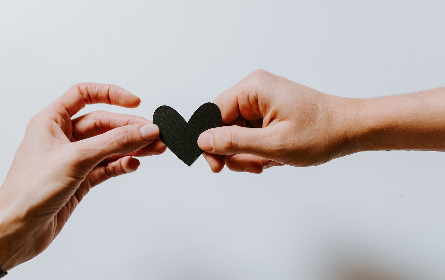 a small paper black heart held by the hands of two people