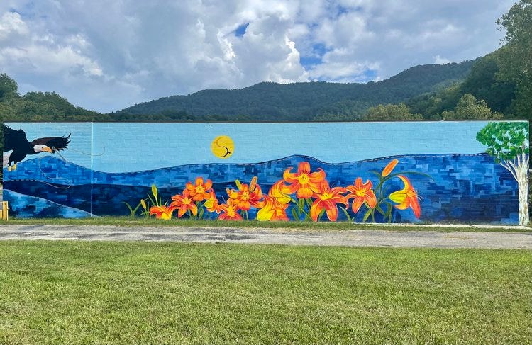 mural on wall beneath vista of mountains shows mountains, an eagle flying and brilliant yellow and orange day lilies. 